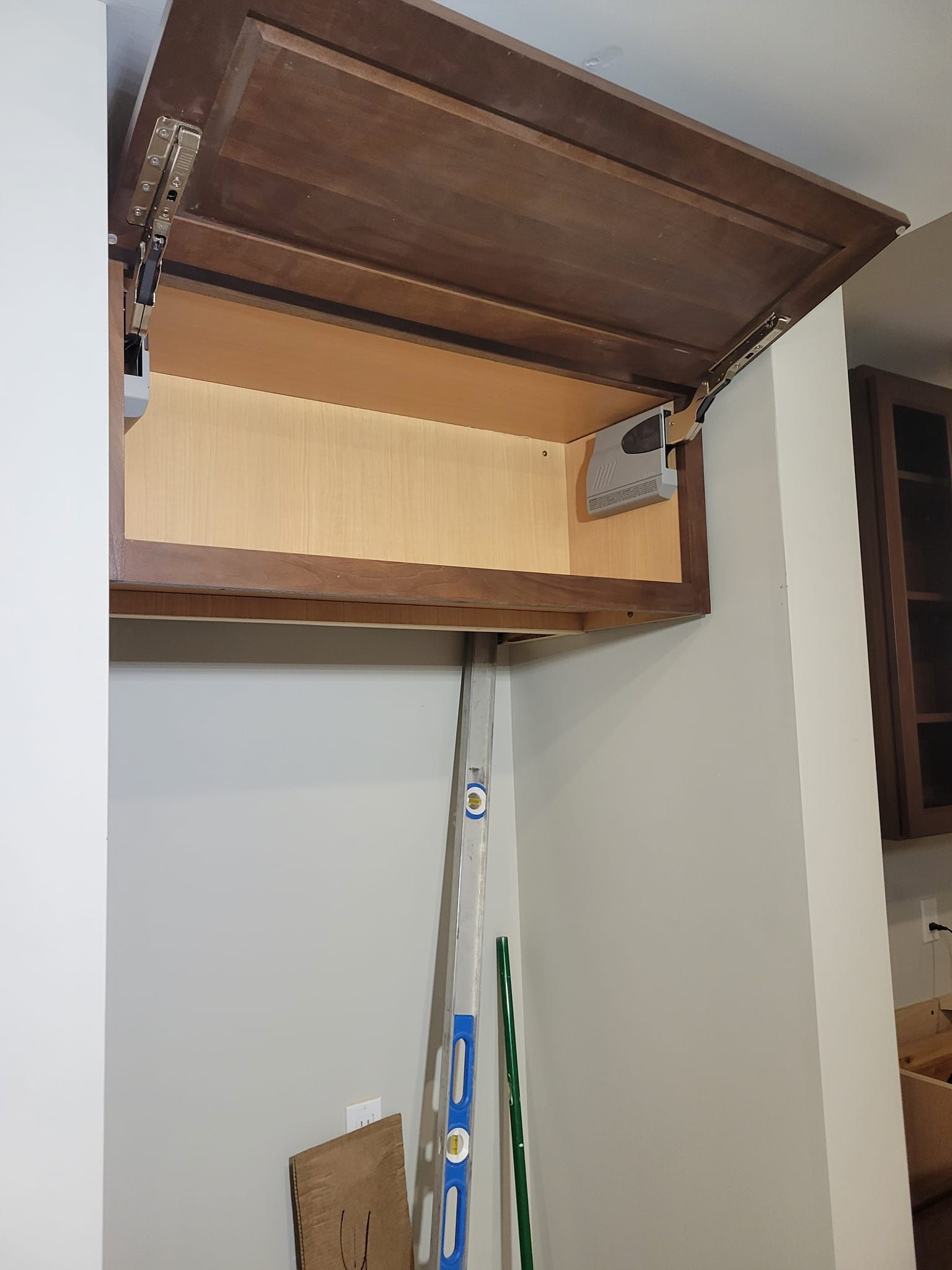 Open kitchen cabinet with upward-opening door; light interior, dark brown exterior.