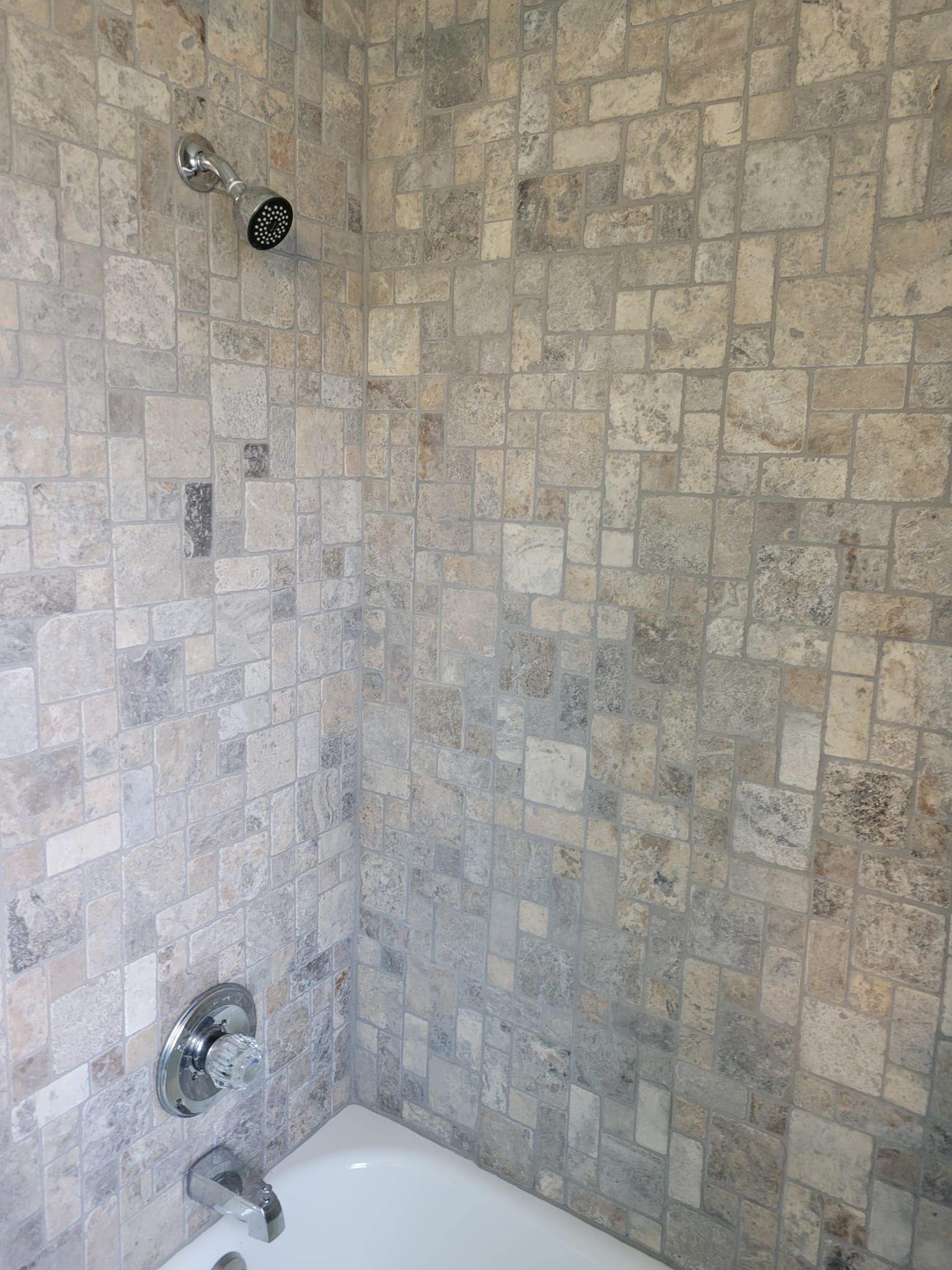 Shower with gray and beige square tile, chrome fixtures, and a white tub.