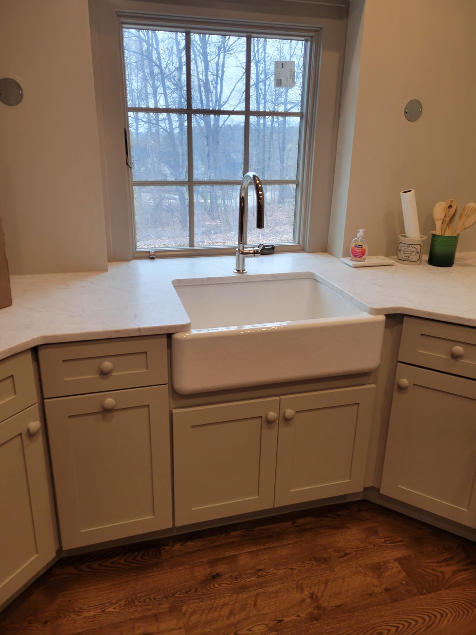 Kitchen with white farmhouse sink under a window, white cabinets, and light countertops.