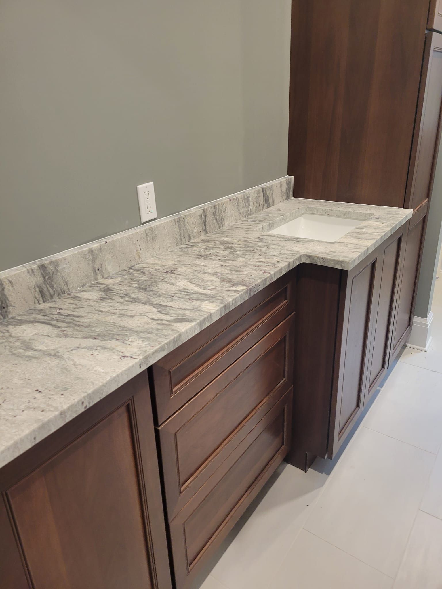 Brown cabinets with gray granite countertop and white sink.