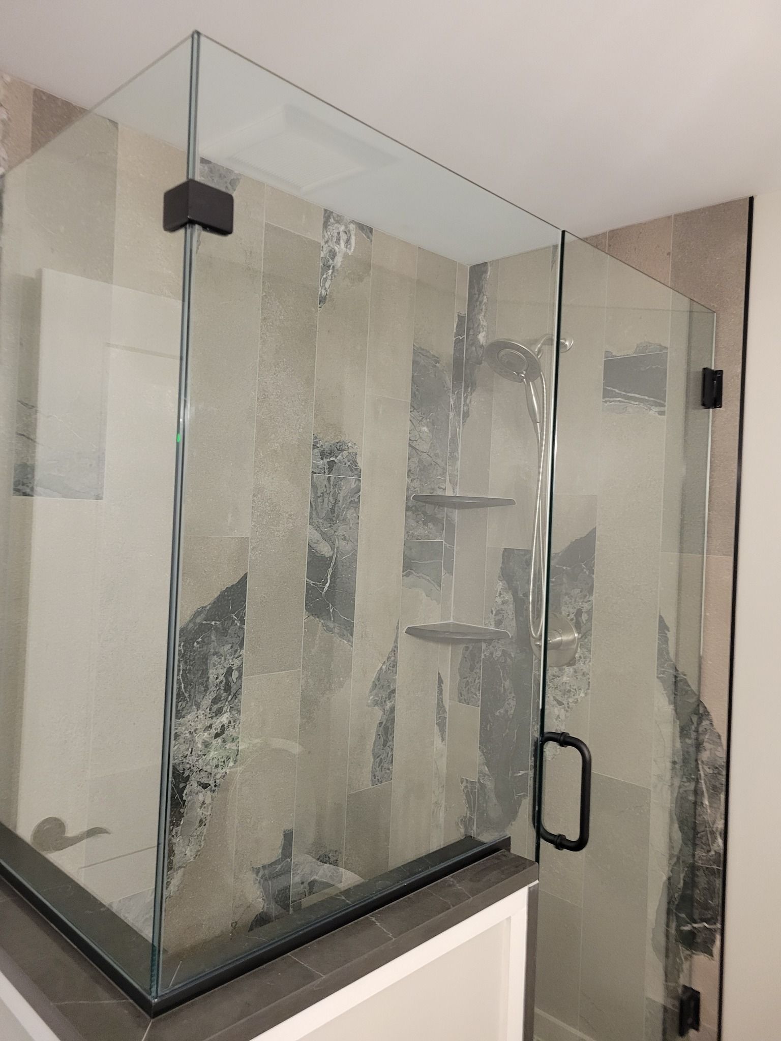 Glass shower enclosure with black hardware, decorative tile background.