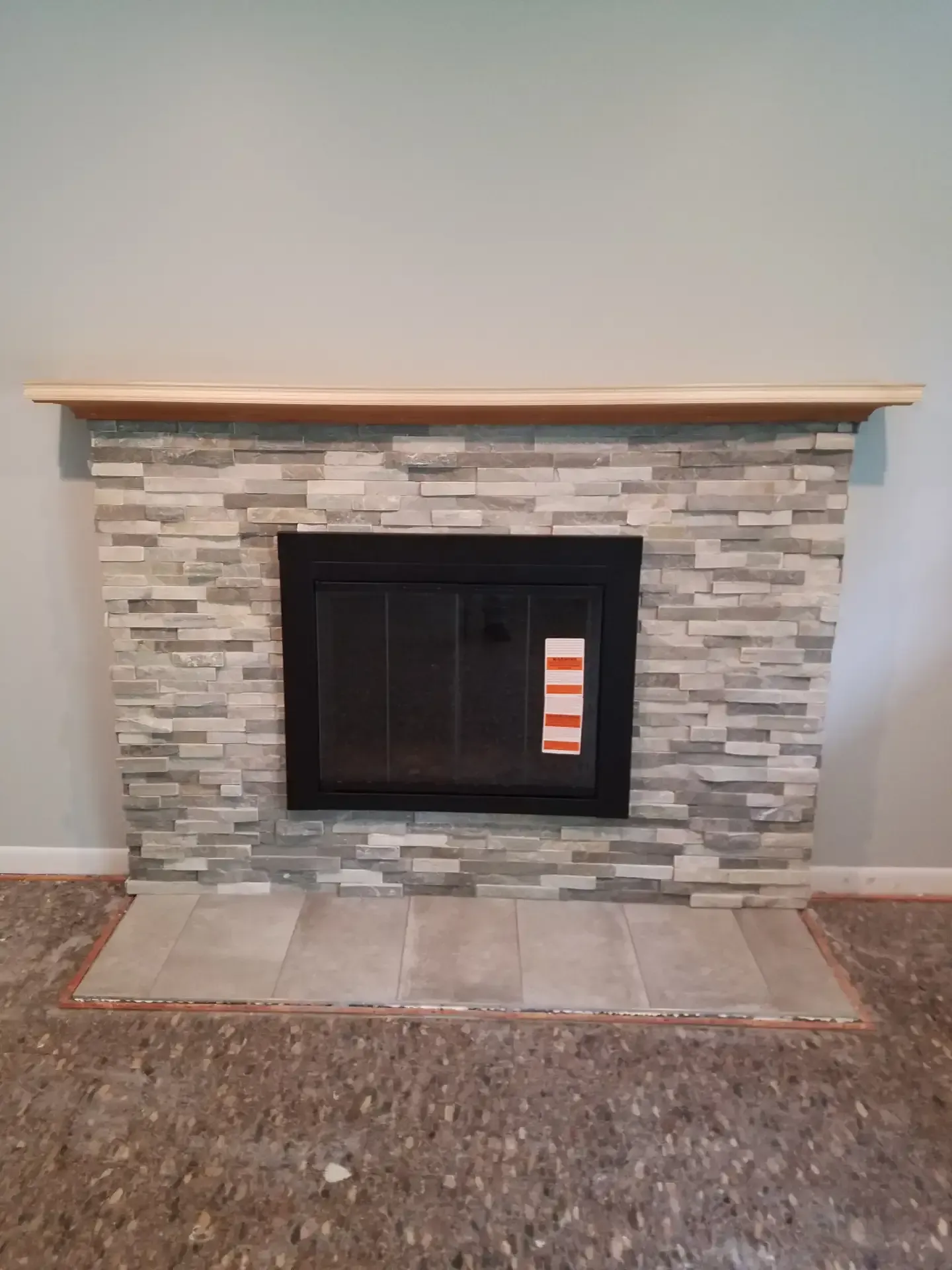 Fireplace with gray stone tile surround and wooden mantel. Black fireplace insert with new tile hearth.
