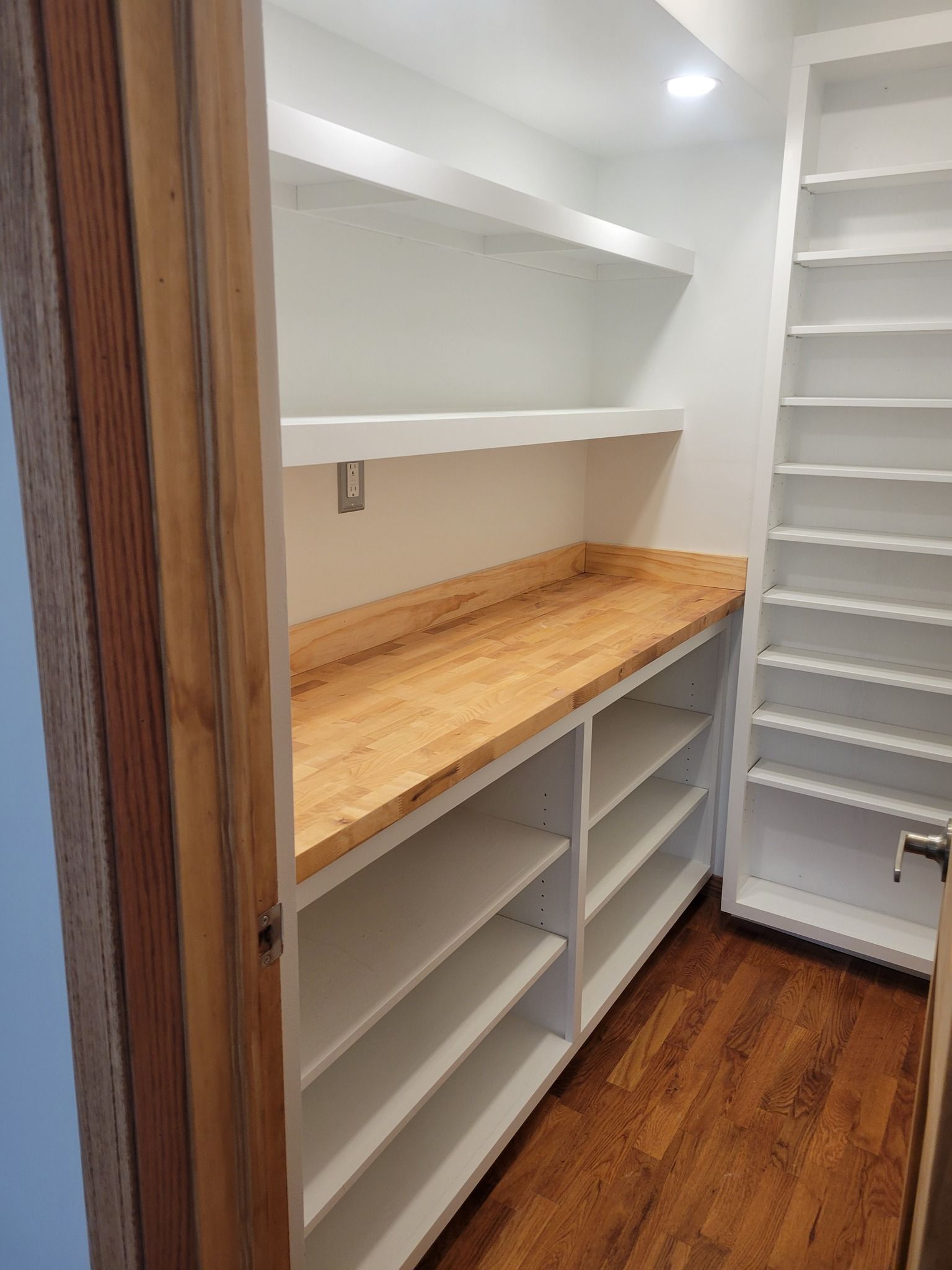 Pantry with wooden countertop, white shelves, and white cabinets. Wooden floor and doorframe.