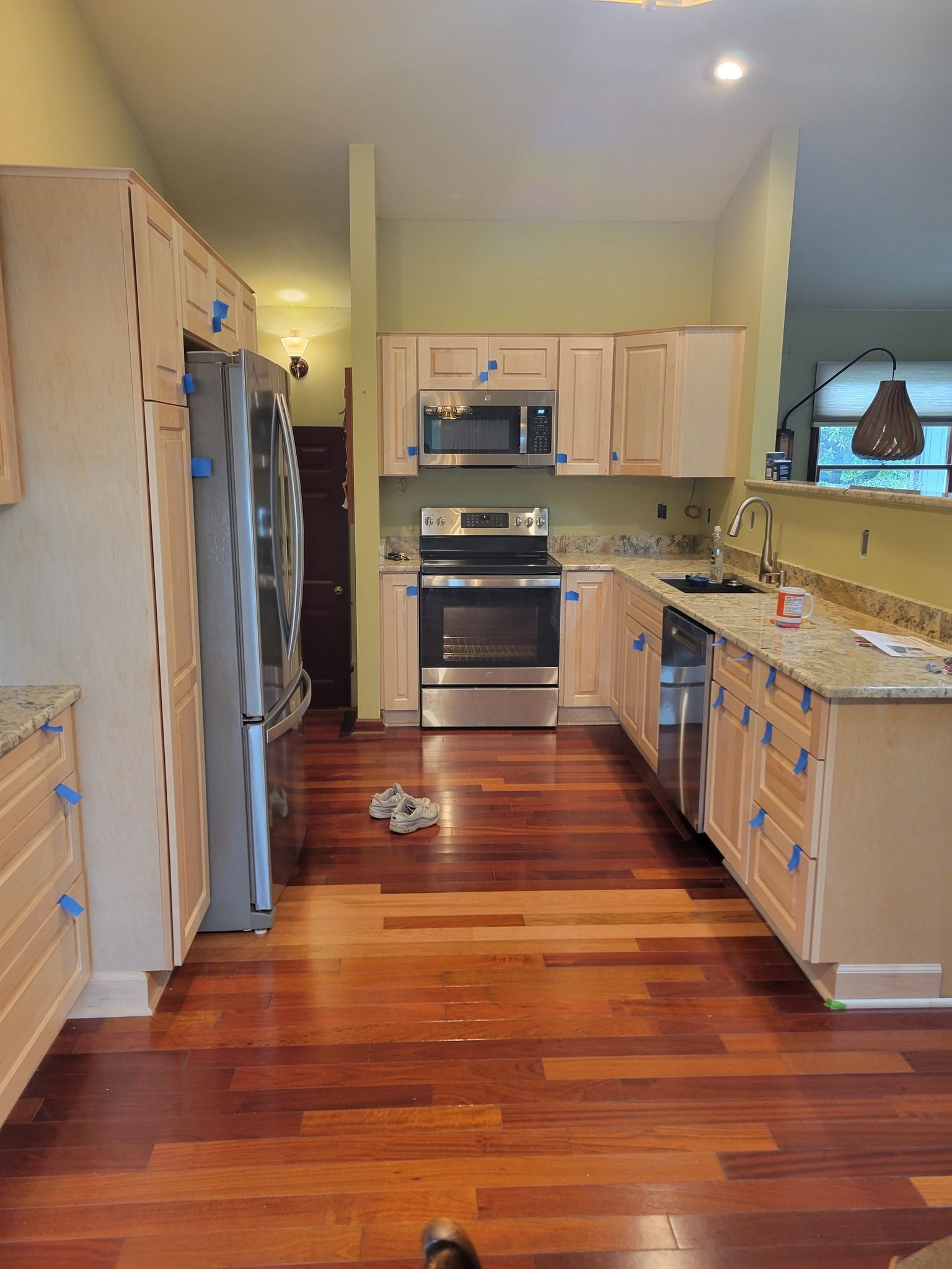 Kitchen remodel: light wood cabinets with blue tape, stainless steel appliances, and brown hardwood floors.