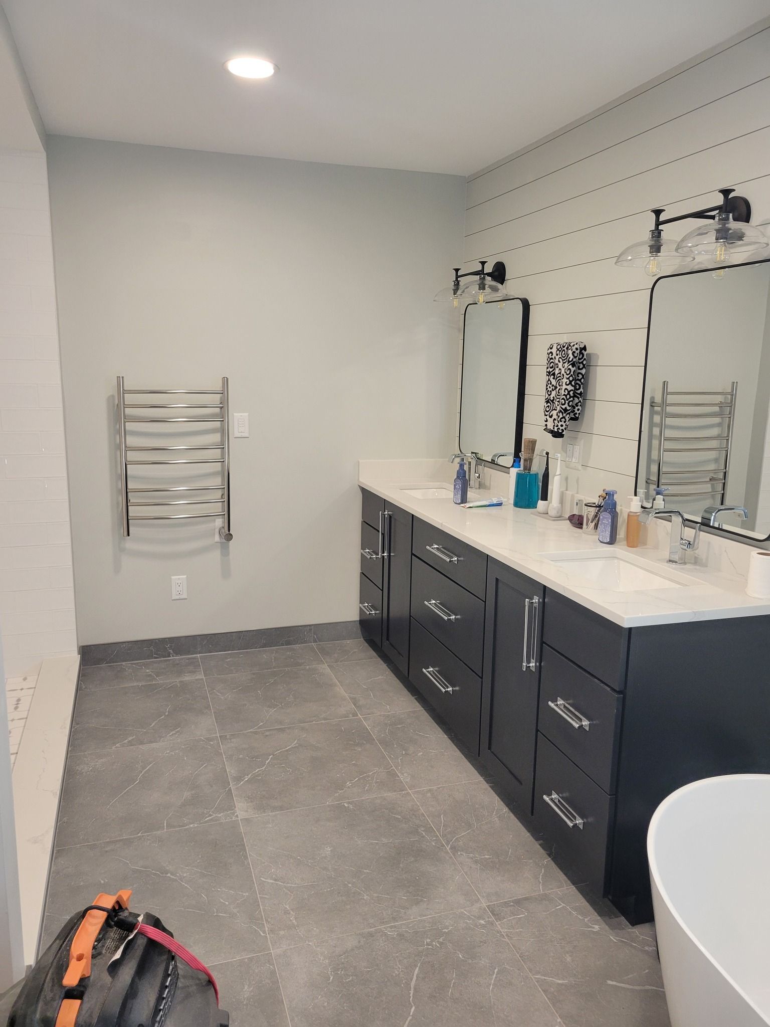 Bathroom with a dark blue vanity, two mirrors, and a heated towel rack. Gray tiled floor.