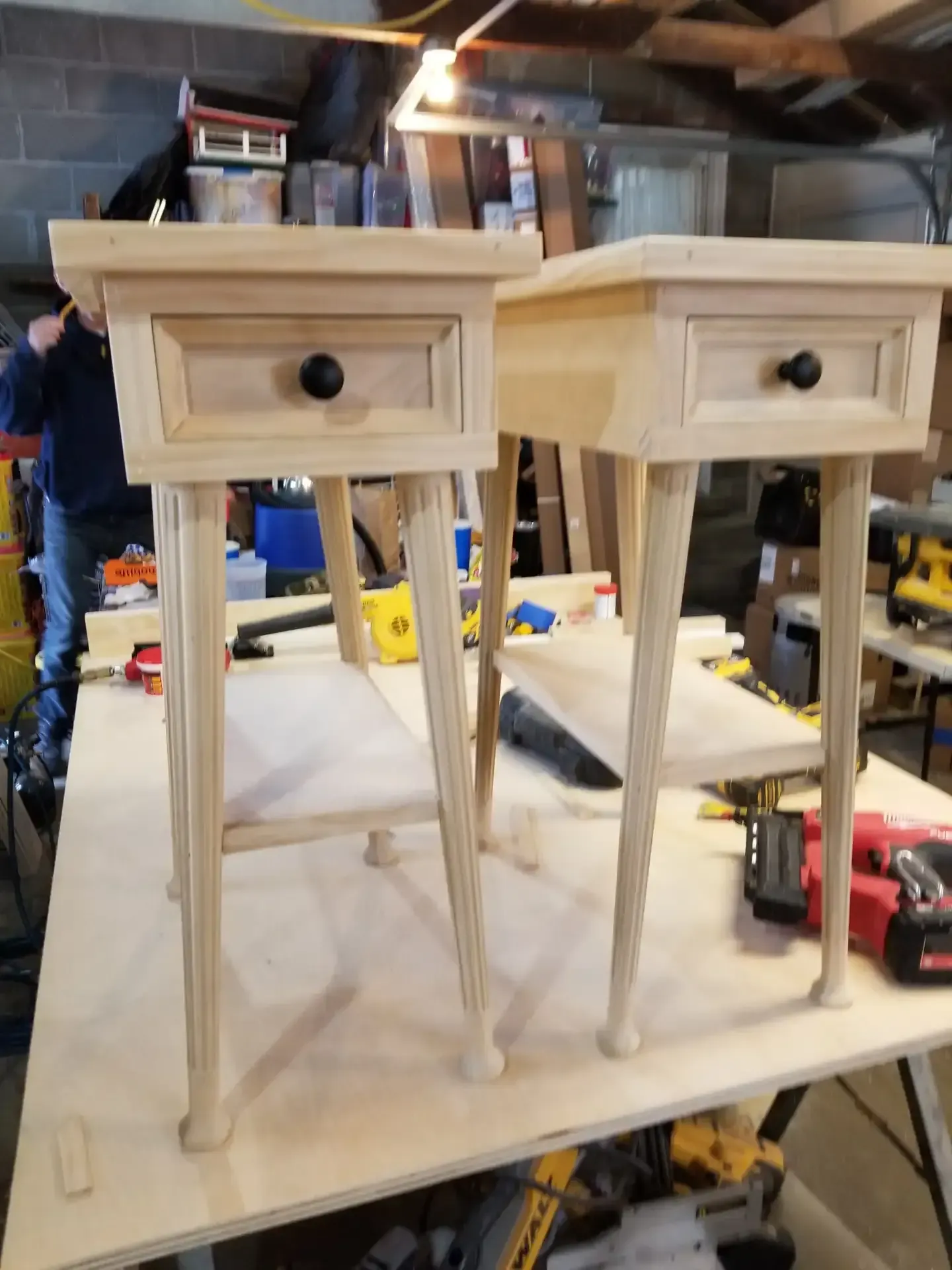 Two unfinished wooden nightstands with drawers, on a workbench in a workshop.