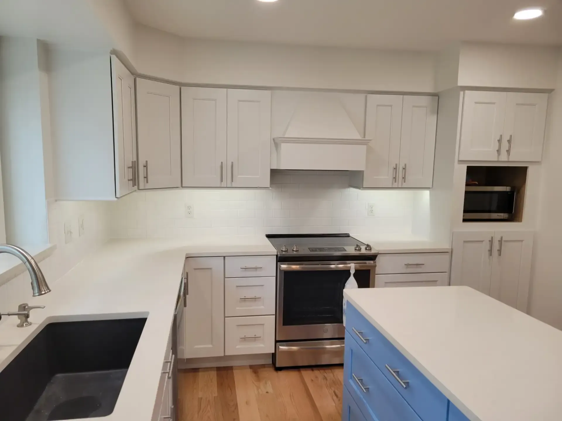 White kitchen with blue island, stainless steel appliances, and wooden floor.