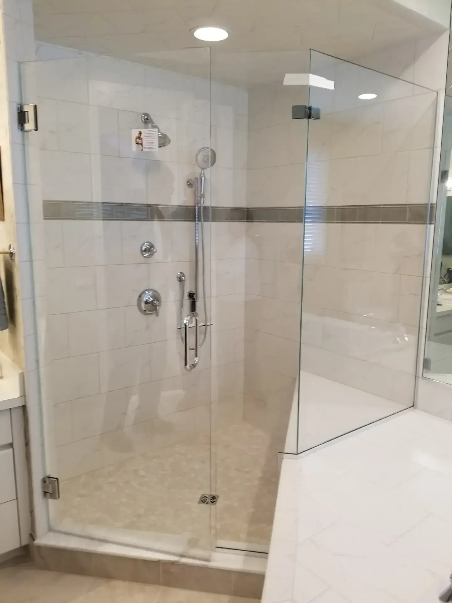 Glass shower enclosure with gray accent tile, and chrome fixtures in a bathroom.