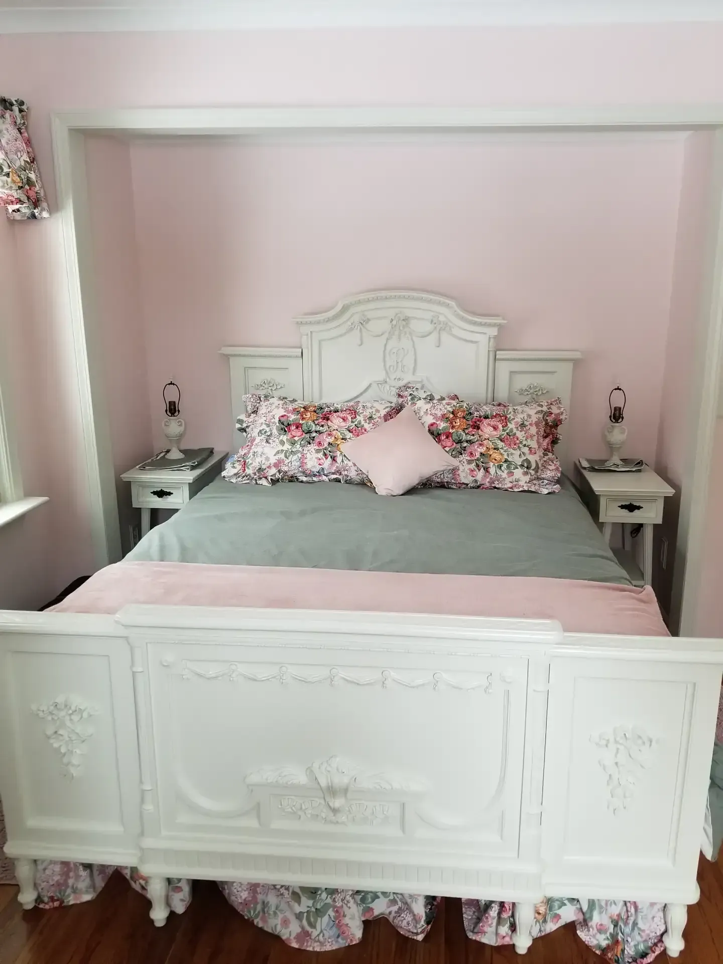 White bed with floral bedding in a pink room; two bedside tables with lamps.