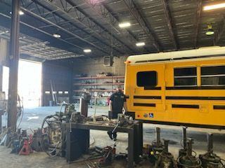 A man is working on a yellow school bus in a garage – Fairfield, AL - Big Moe Spring & Alignment of B'Ham