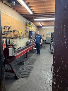 A man is standing in a garage next to a lathe – Fairfield, AL - Big Moe Spring & Alignment of B'Ham