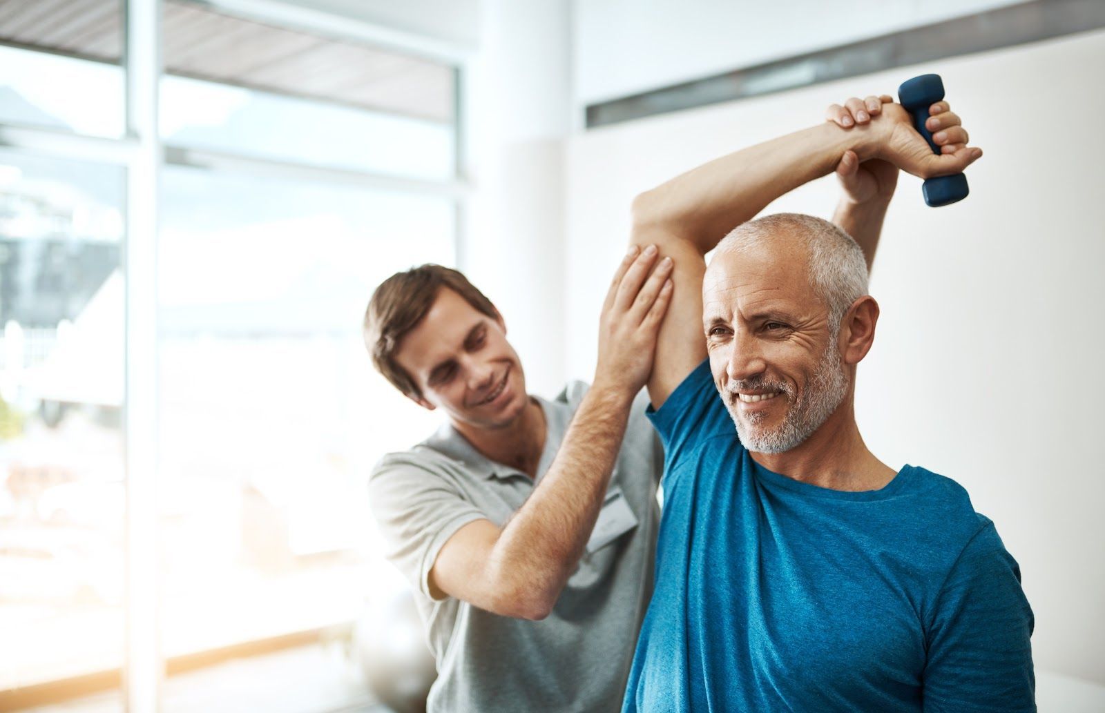 Therapist assisting a patient's arm exercise with a dumbbell in a bright room.