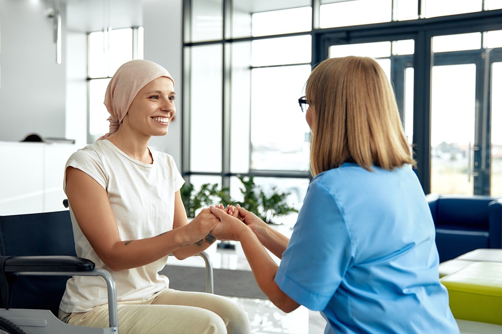 Woman with headscarf smiles, holding hands with a nurse in a medical setting.