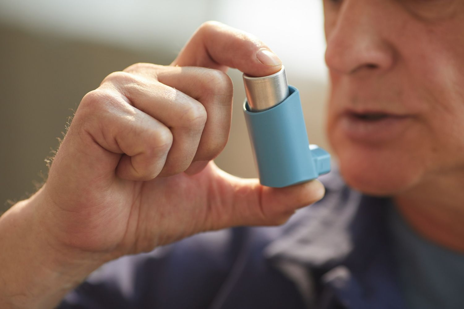 A man is holding a blue inhaler in his hand.