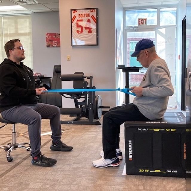 Man and therapist use resistance band during therapy session. Indoor setting.