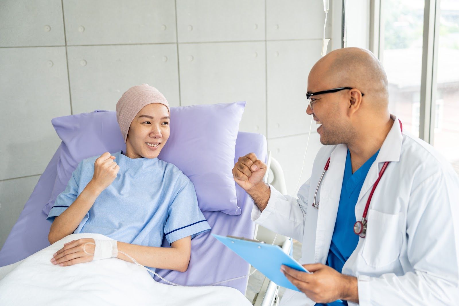 Woman in hospital bed with doctor, both smiling and gesturing, in a bright room.