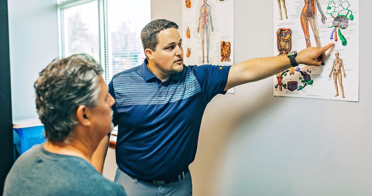 A man is pointing at a poster on a wall while talking to another man.