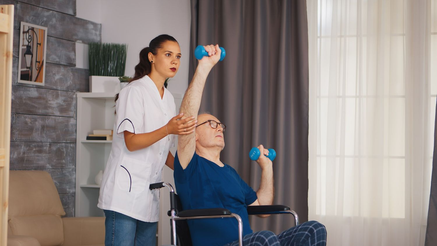 Caregiver assisting seated patient with dumbbells during home physical therapy exercise