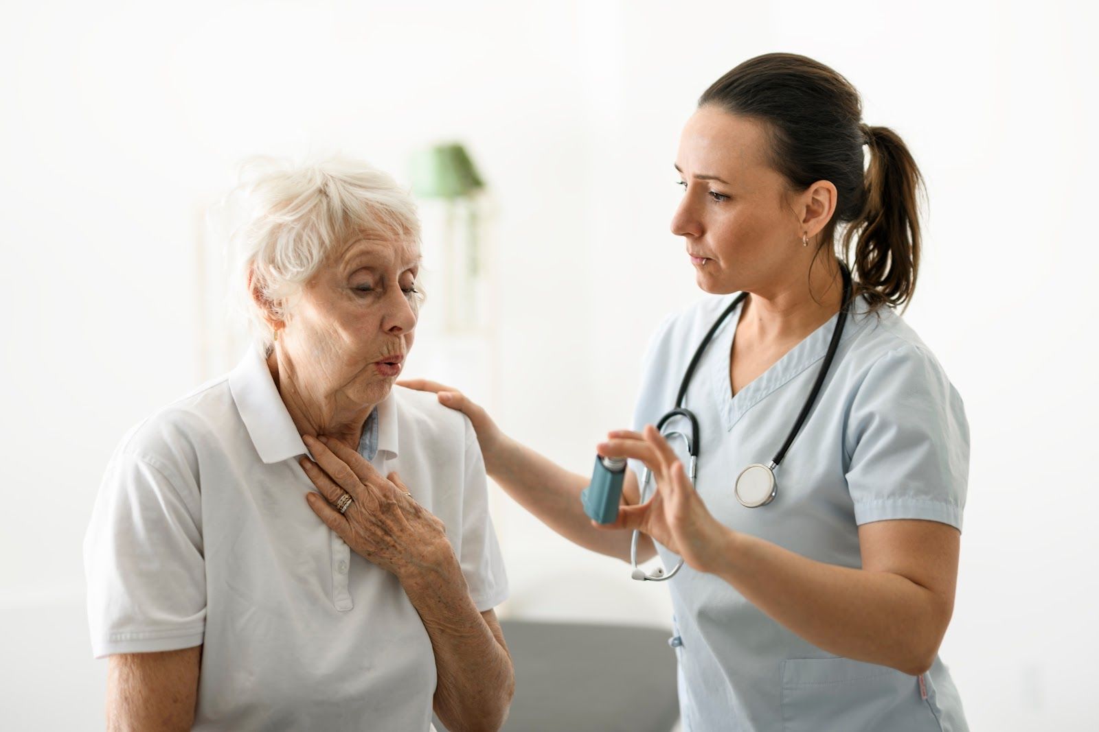 Nurse assisting elderly patient with asthma inhaler; indoor setting.