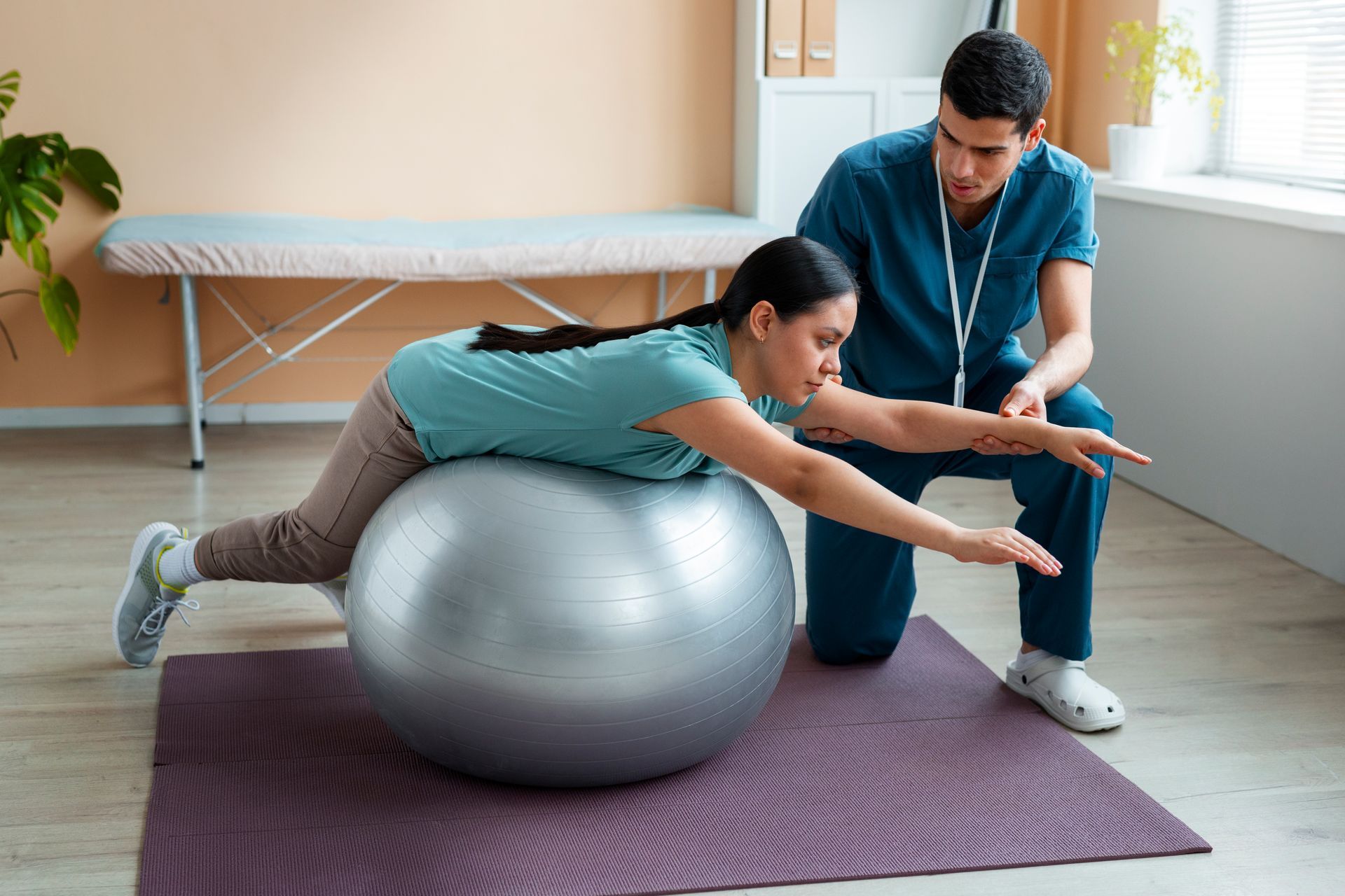 A pregnant woman is doing exercises on an exercise ball with a nurse.