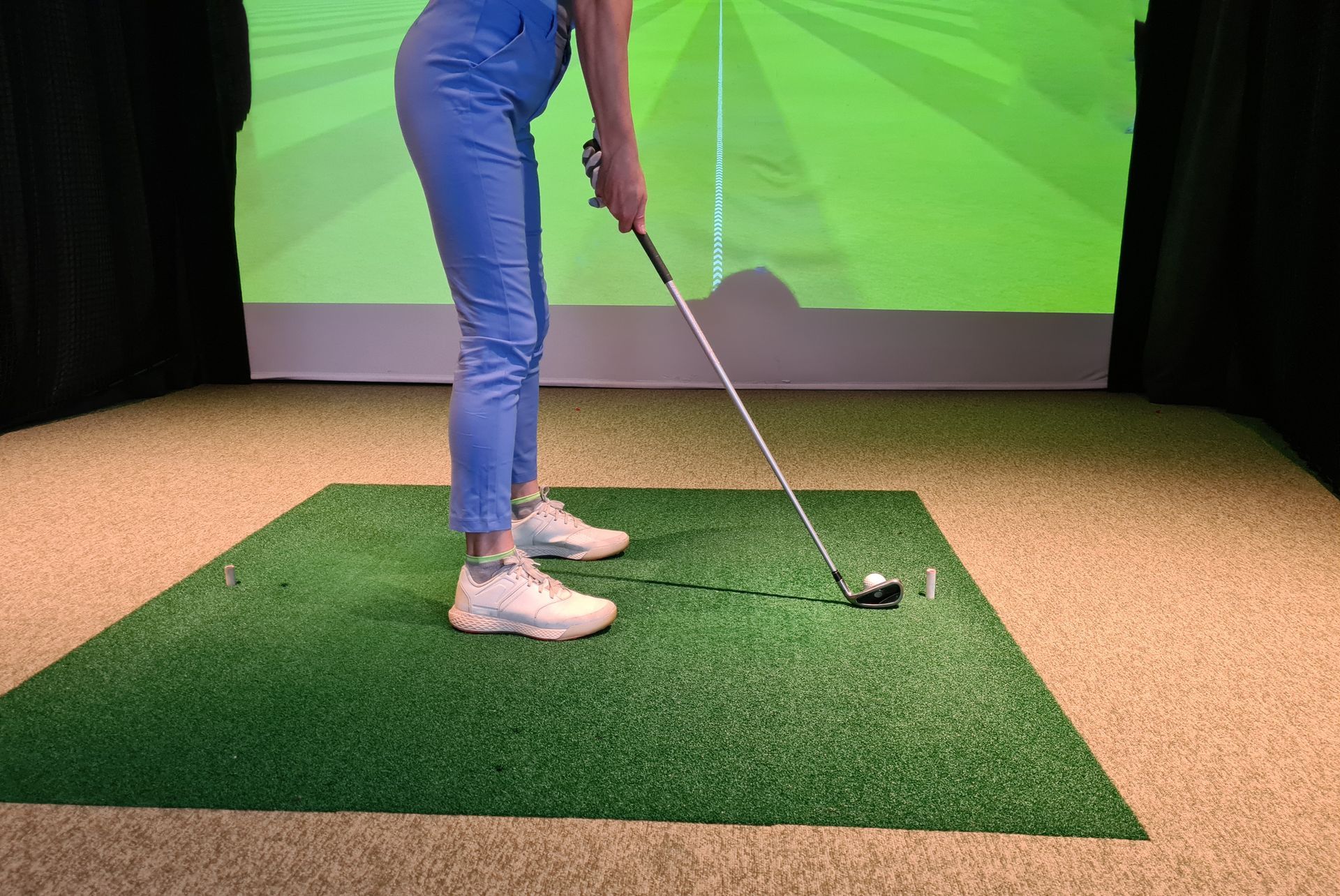 A woman is swinging a golf club at a golf ball in a simulator.