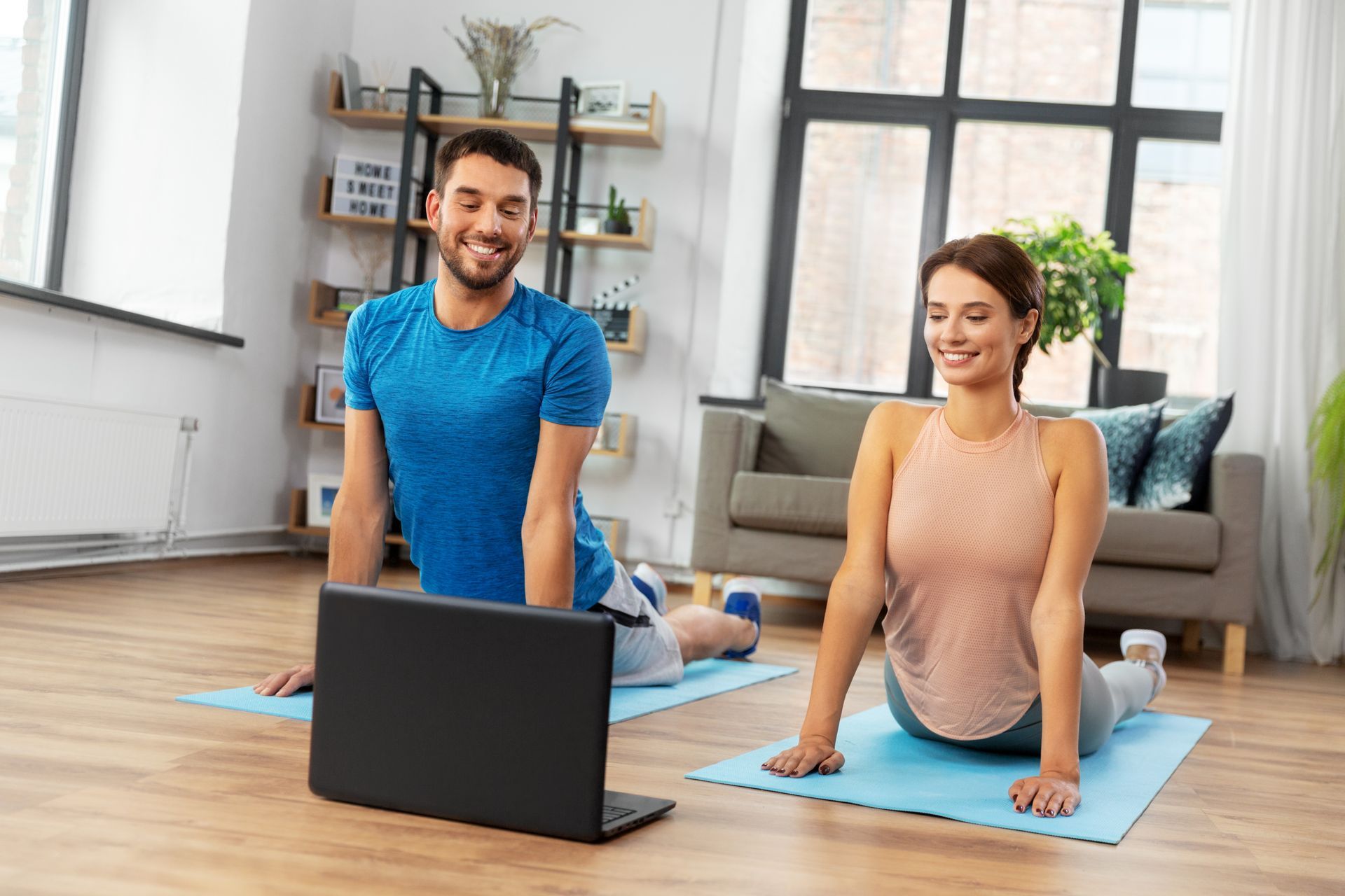 A man and a woman are doing yoga in front of a laptop computer.