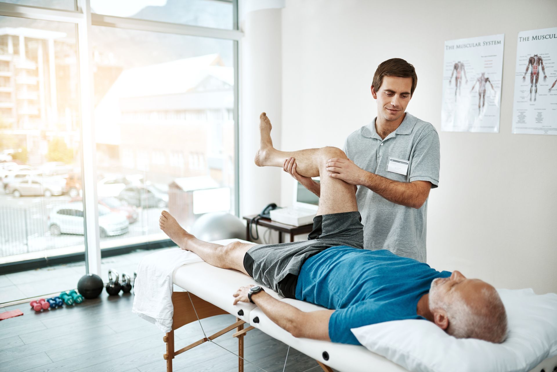 Physical therapist working with a patient on a table, extending the patient's leg; indoor clinic.