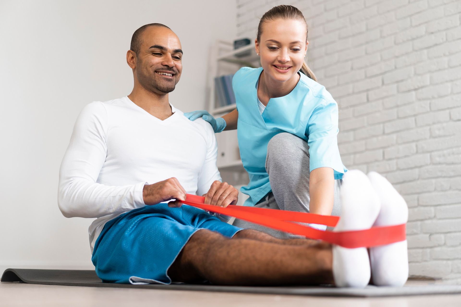 A woman is helping a man stretch his legs with a resistance band.