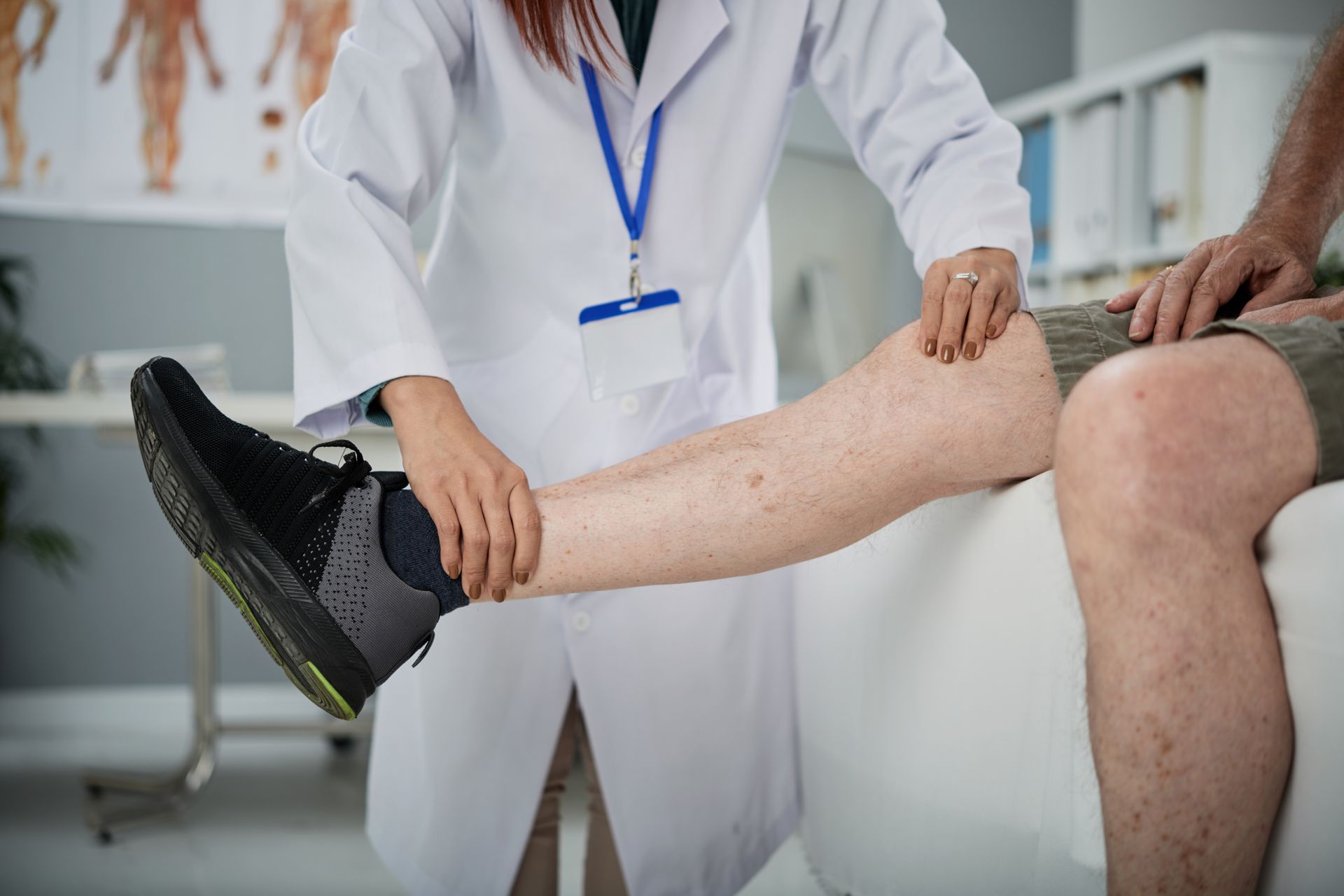 Doctor examining a patient's leg in a medical setting. Doctor is wearing a white coat, patient is seated.