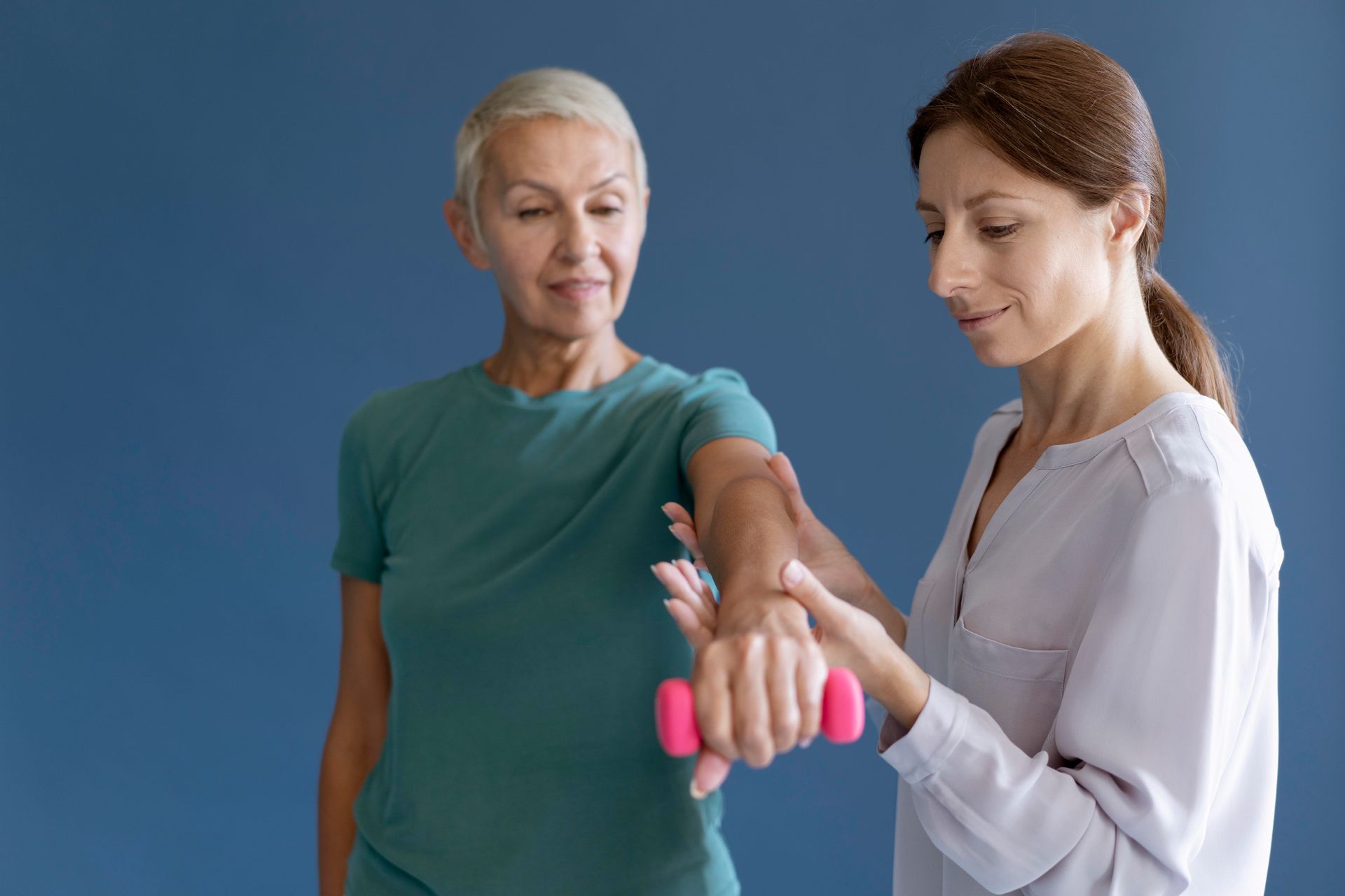 A woman is helping an older woman lift a pink dumbbell.