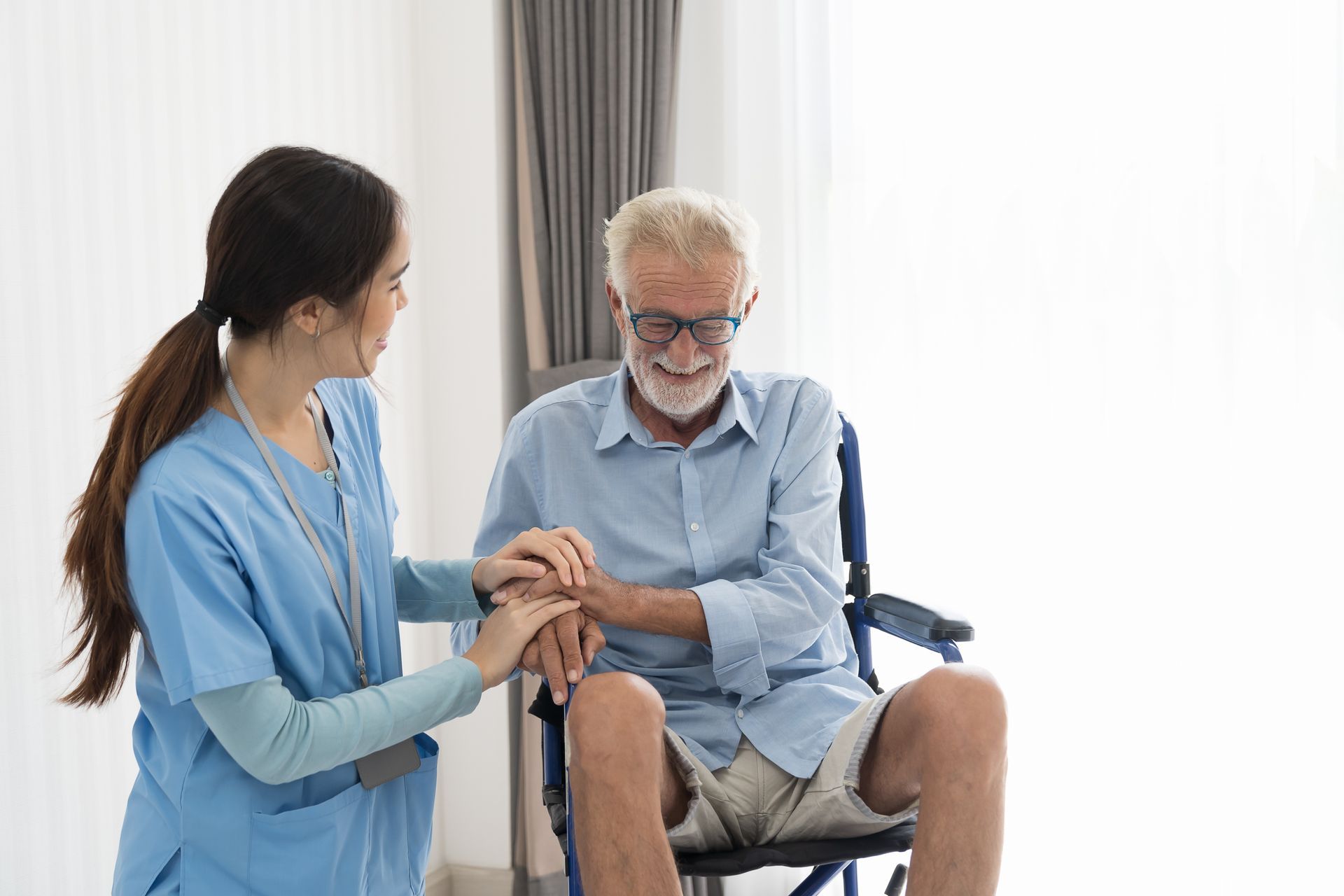 A nurse is holding the hand of an elderly man in a wheelchair.