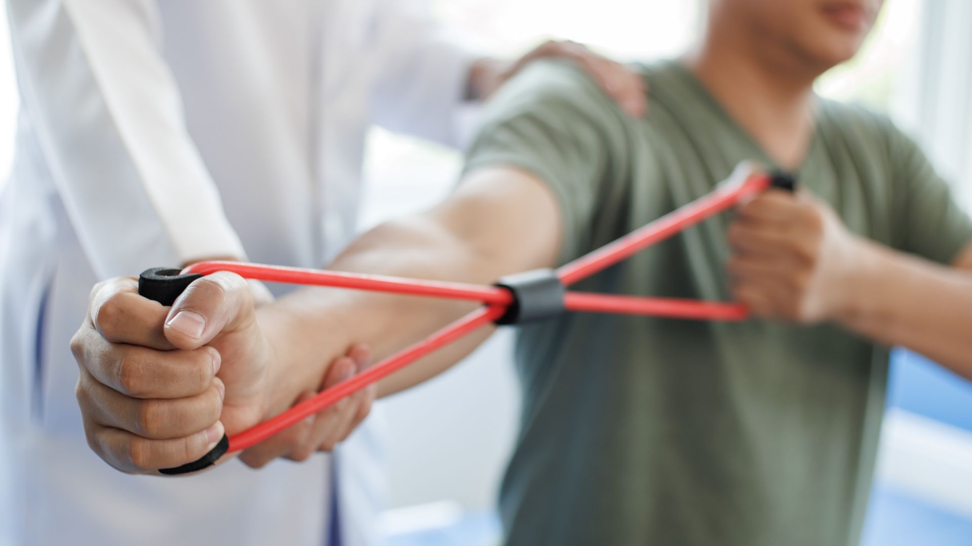 A man is being helped by a doctor to stretch his arms with a rubber band.