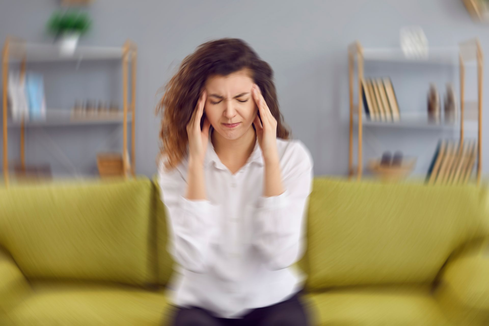 A woman is sitting on a green couch with a headache.