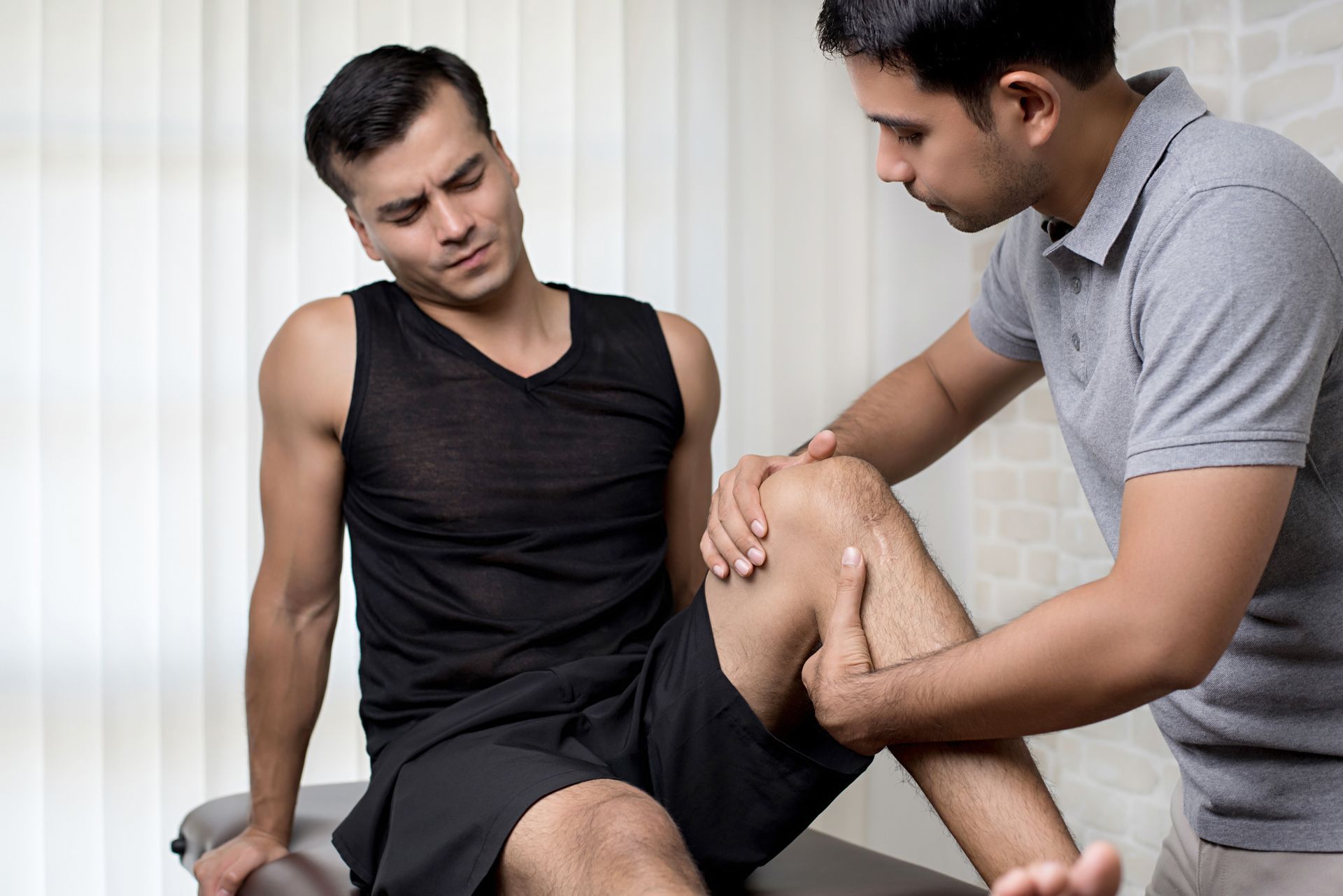 A man is sitting on a table while a doctor examines his knee.