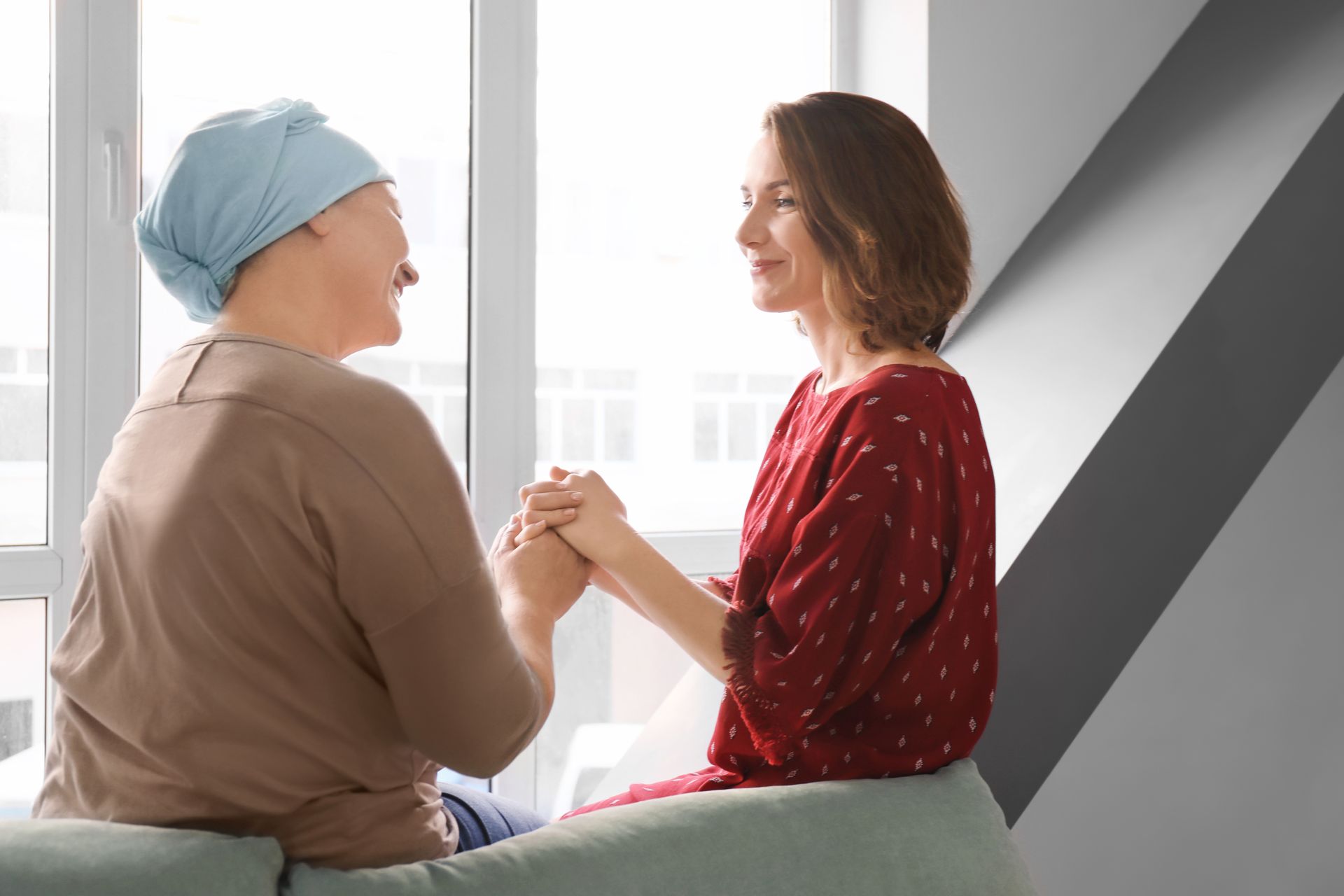 A woman is holding the hand of a woman with cancer while sitting on a couch.