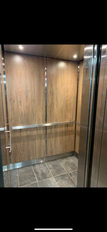 L'intérieur d'un ascenseur avec des murs en bois et des poignées en acier inoxydable.