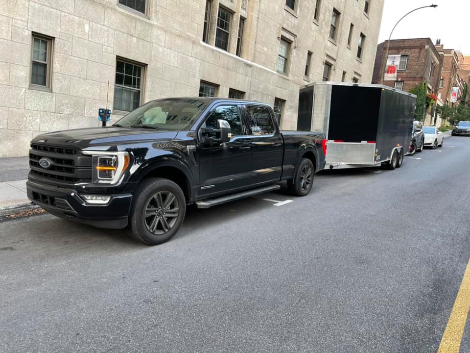 Un camion noir est garé sur le bord de la route à côté d'une remorque.