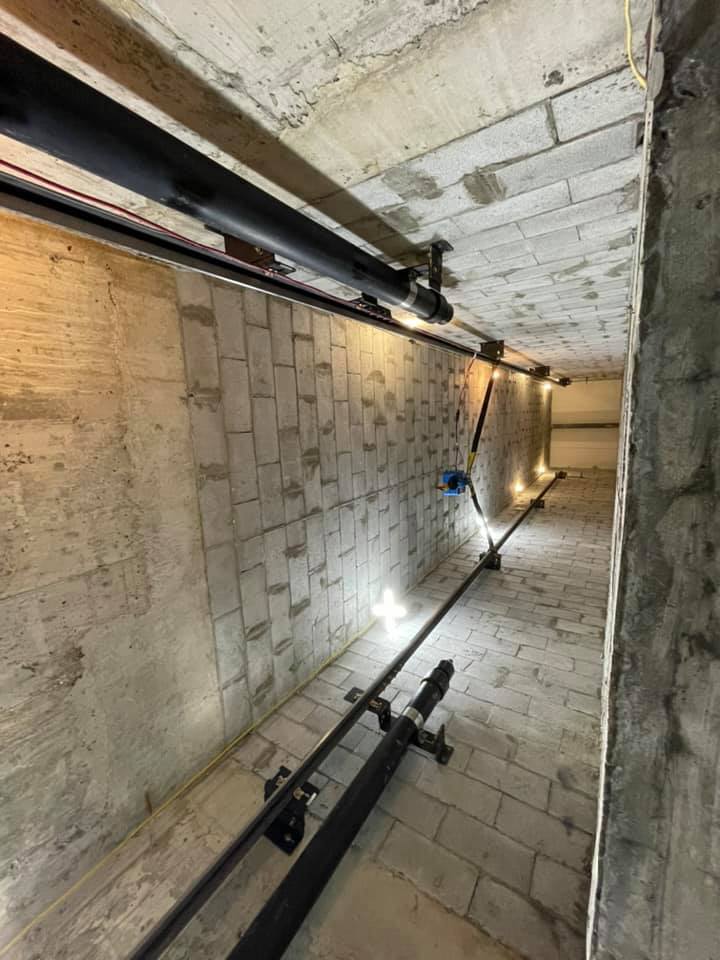 Un tunnel traversé par des tuyaux et un mur de briques.