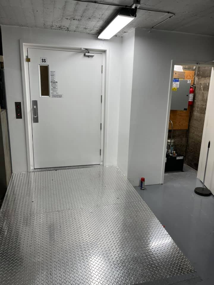 Un couloir avec une porte blanche et un sol en métal.