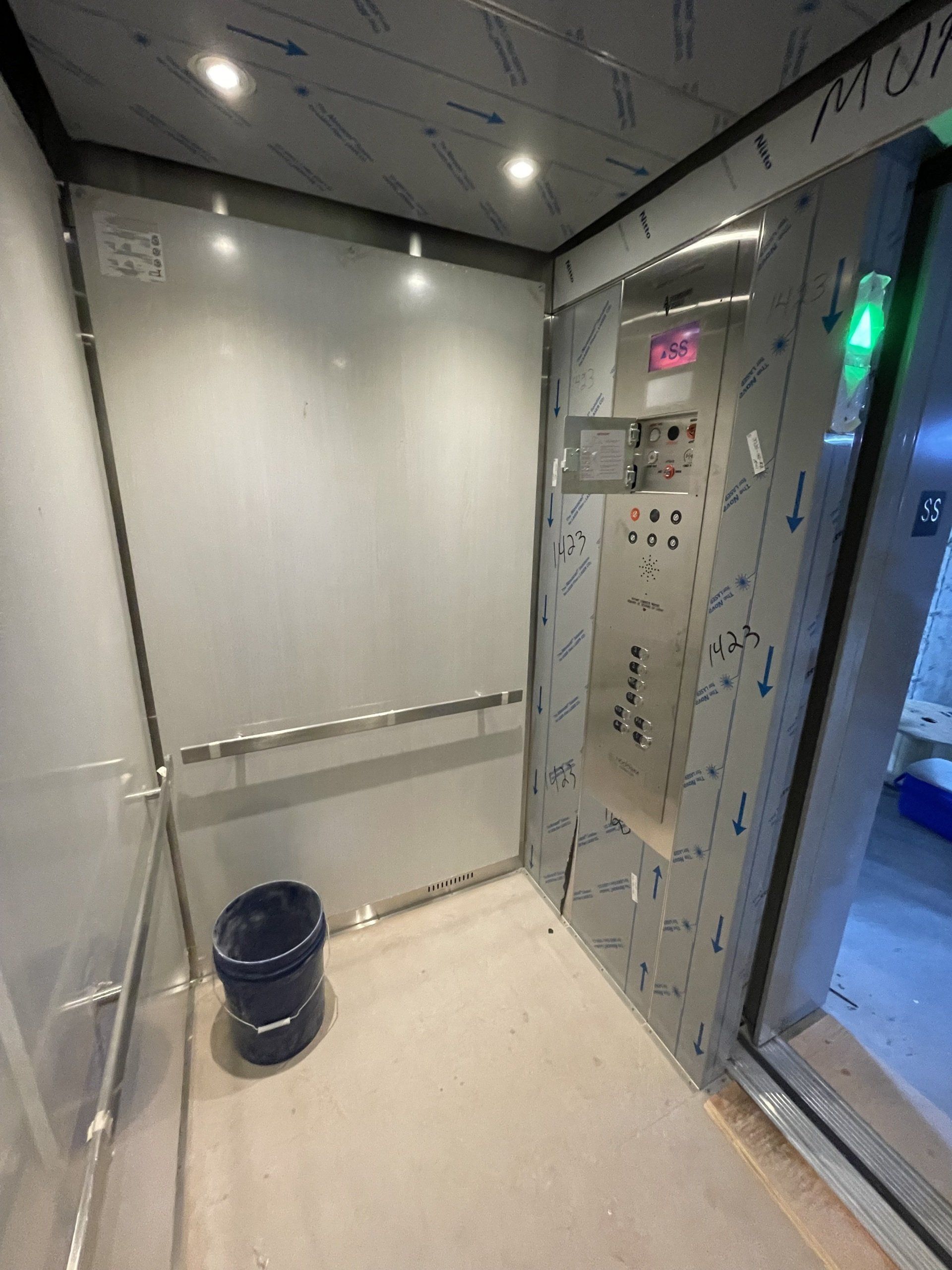 L'intérieur d'un ascenseur avec un seau bleu au sol.