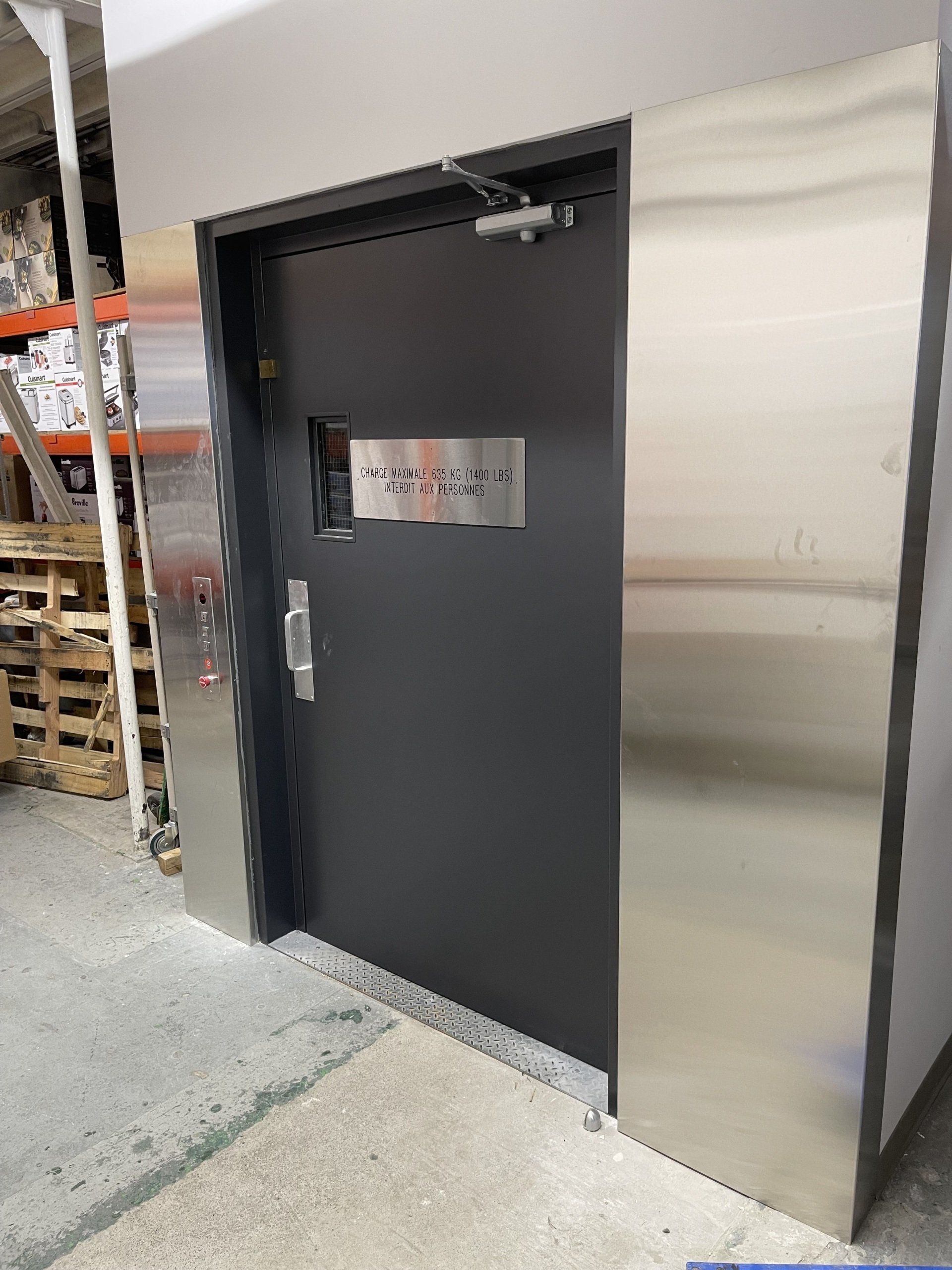 Une porte noire avec une garniture en acier inoxydable se trouve dans un entrepôt.