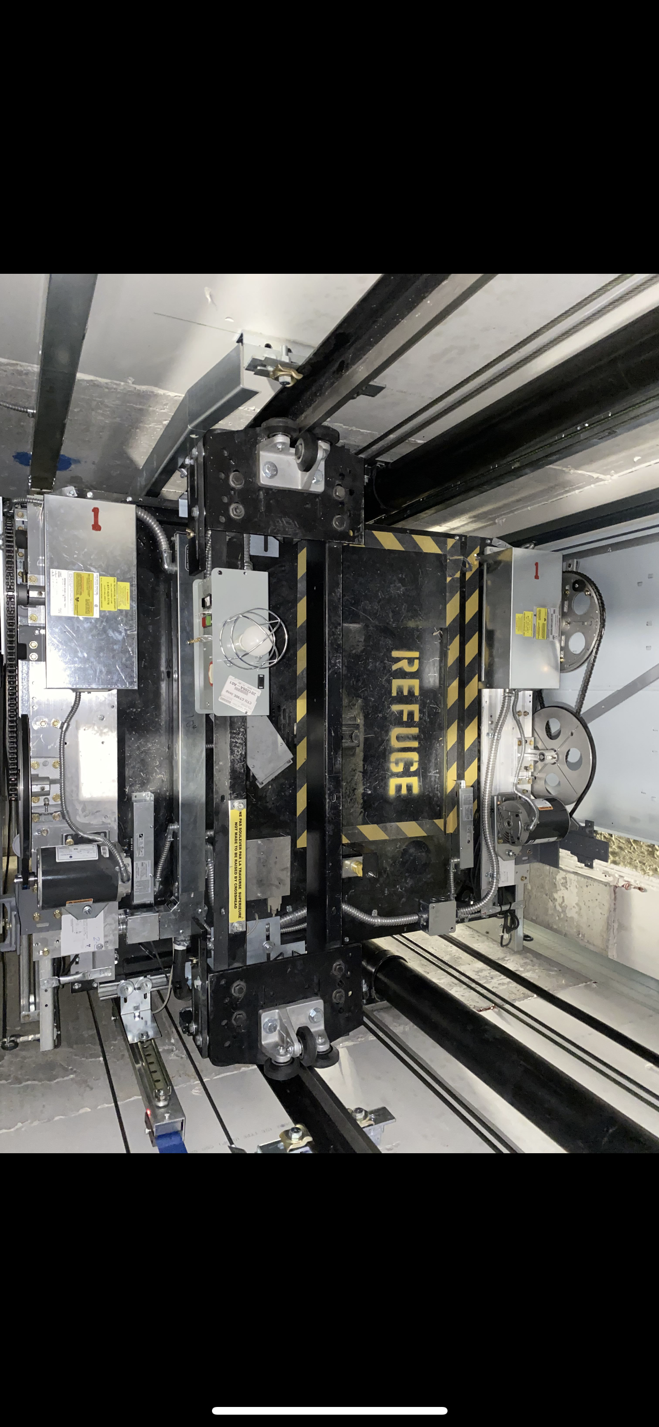 Intérieur d'un ascenseur, portes ouvertes, révélant un couloir blanc. Panneau en acier inoxydable avec boutons.