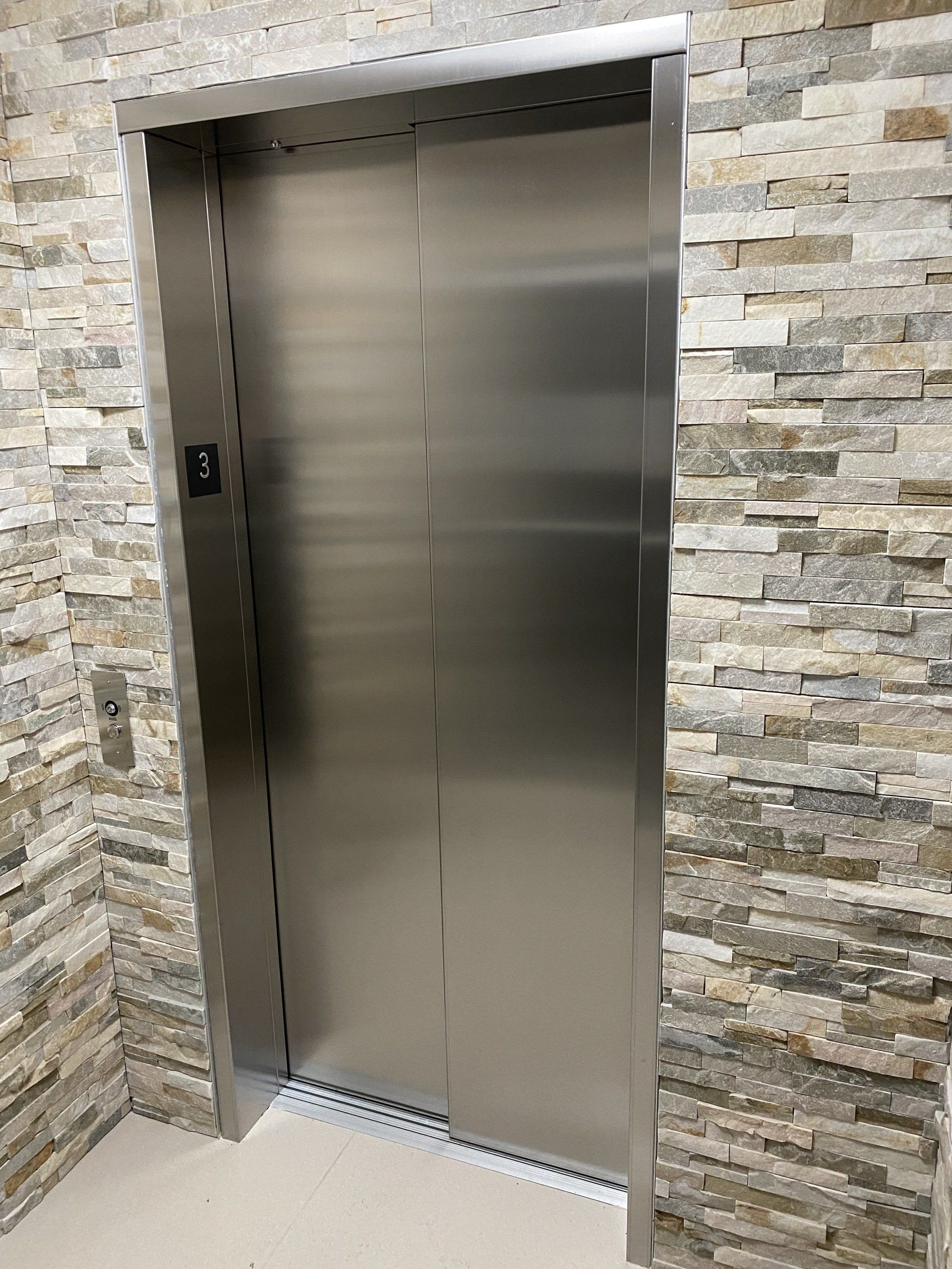 Une porte d'ascenseur en acier inoxydable avec un mur de briques en arrière-plan.