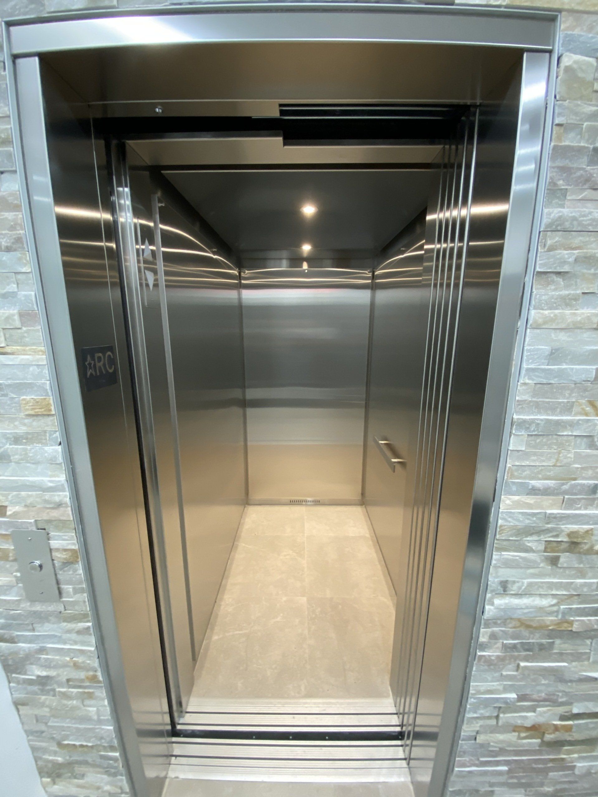 Un ascenseur en acier inoxydable avec un mur de pierre derrière lui