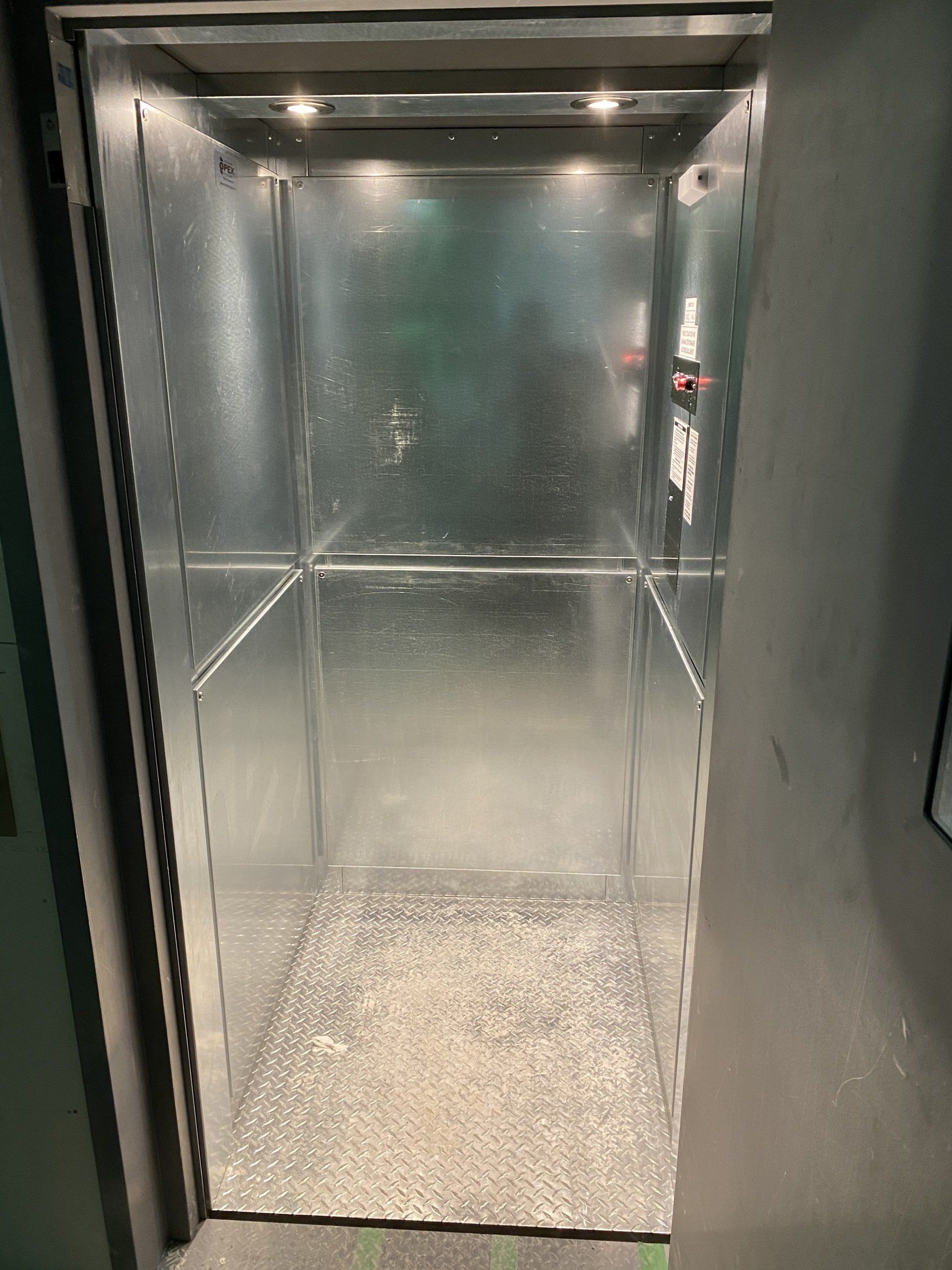 Cabine d'ascenseur en métal vide avec éclairage au sol et au plafond texturé.