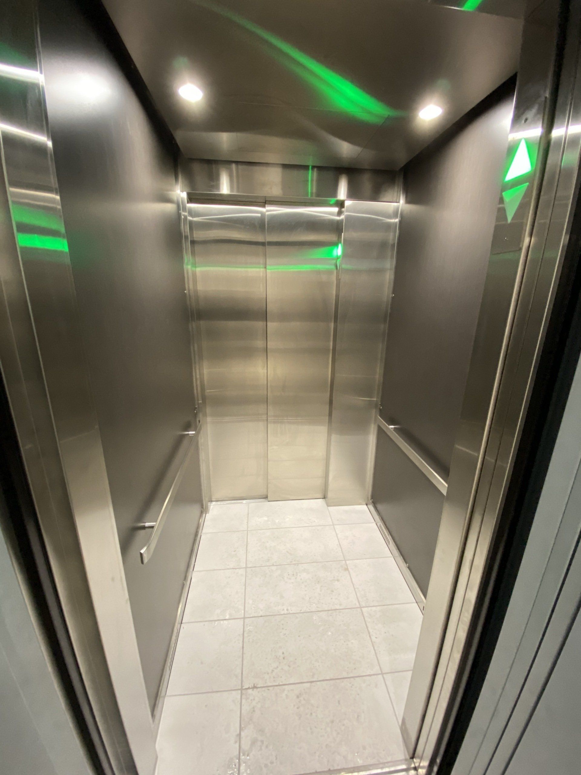 Un ascenseur en acier inoxydable avec une lumière verte au plafond.