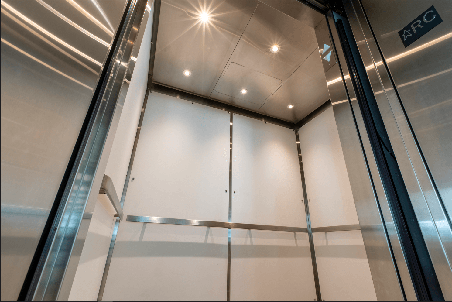 À l'intérieur d'un ascenseur avec des garnitures en acier inoxydable, des murs blancs et des plafonniers.