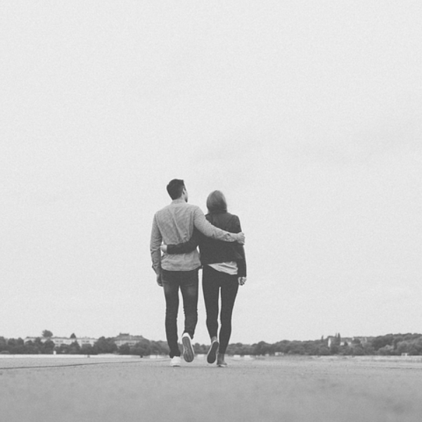 A man and woman walk together arm in arm on a path, looking towards the horizon. Black and white.