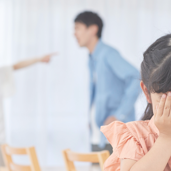 Girl covering ears, parents arguing in background.