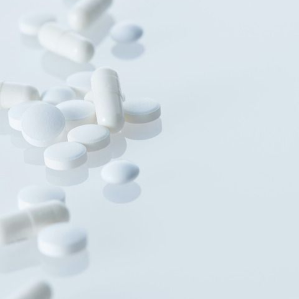 White pills and capsules scattered on a white, reflective surface.
